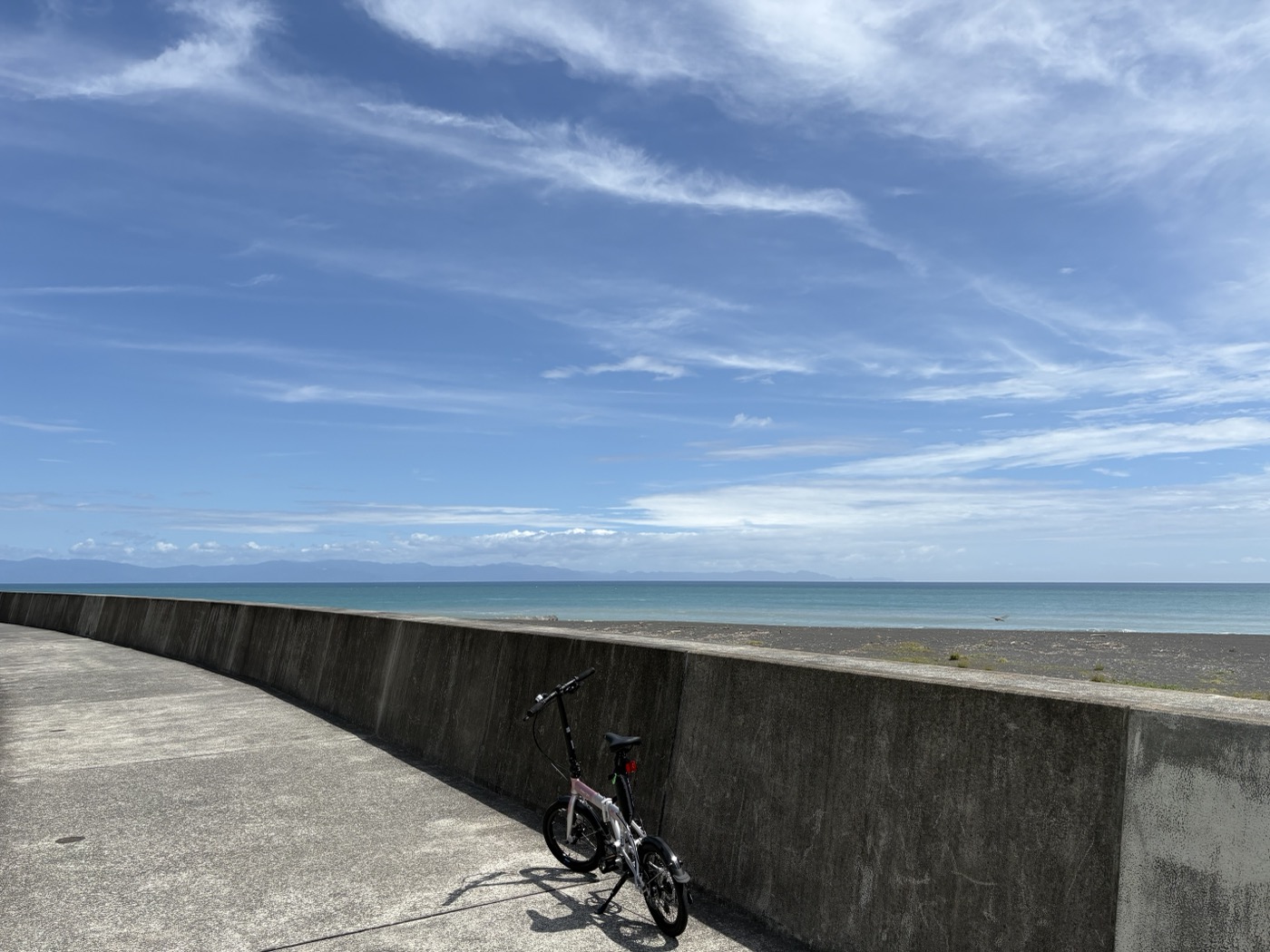 堤防のそばに停めた折りたたみ自転車と海
